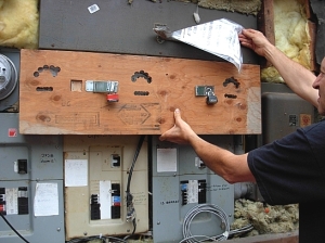 Jurgen shows me the plywood barricade he had  placed over his three remianing analogue meters, with holes cut for meter-reading. BC Hydro broke the locks off the plywood to force a smart meter on him. (Photo © Kim Goldberg)